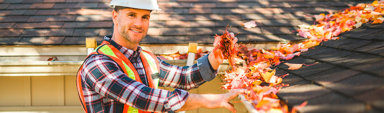 Handwerker mit Helm inspiziert Hausdach und Dachrinne bei Dachrinnenreinigung in Dortmund mit sicherer Steigtechnik.