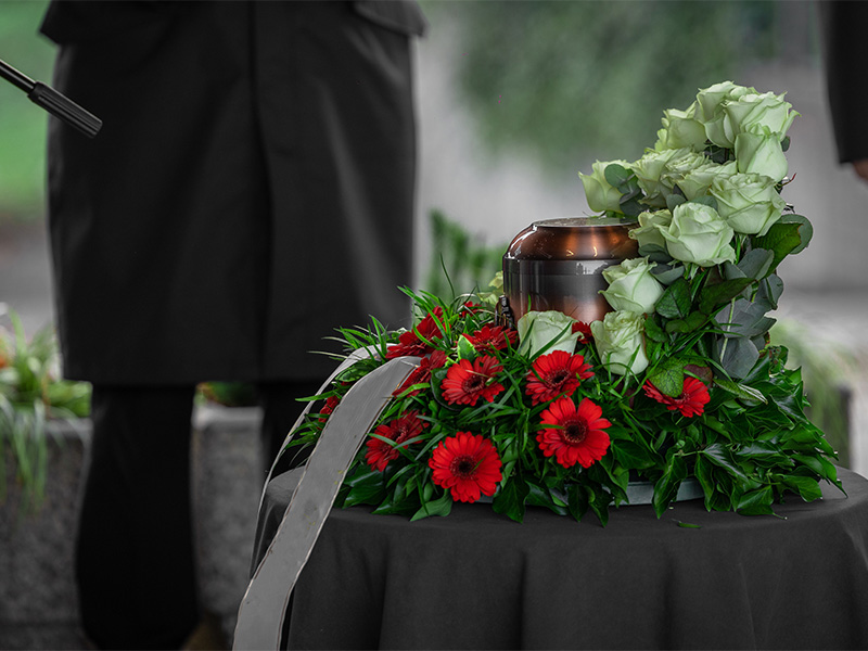 Urne mit Blumenarrangement während einer würdevollen Trauerfeier, Bestatter im Hintergrund bei einer Feuerbestattung in Dortmund.