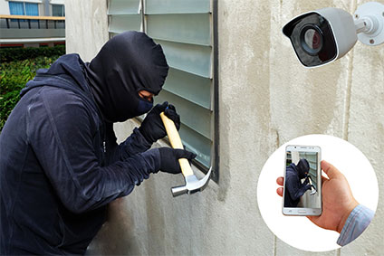 Einbrecher mit Hammer und Maske wird von einer Überwachungskamera gefilmt, die das Bild aufs Smartphone überträgt.