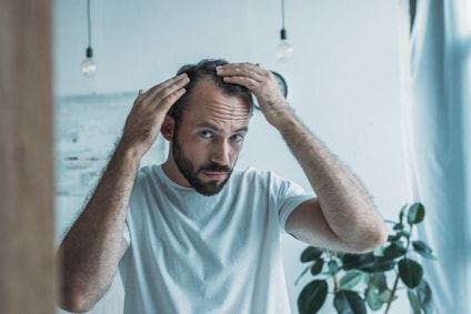 Mann im mittleren Alter mit Haarausfall betrachtet sich im Spiegel