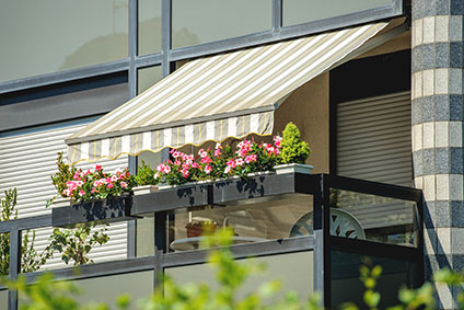 Balkon mit geöffneter Markise und schönen Blumen - an einem warmen Sommertag mit Sonnenschutz abgedeckt