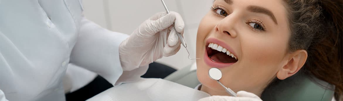 Frau mit offenem Mund guckt in die Kamera in einer Zahnarztpraxis