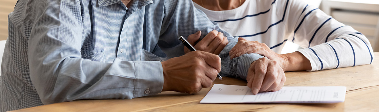 Älteres Paar unterschreibt gemeinsam Dokument zur finanziellen Absicherung und Vorsorgeversicherung in Dortmund bei Beratungsgespräch im Büro
